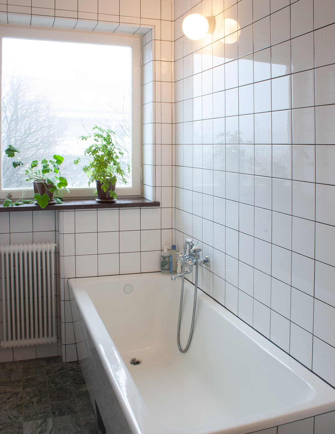 Funkisbadrum med inbyggt badkar med vitt kakel i raka förband.